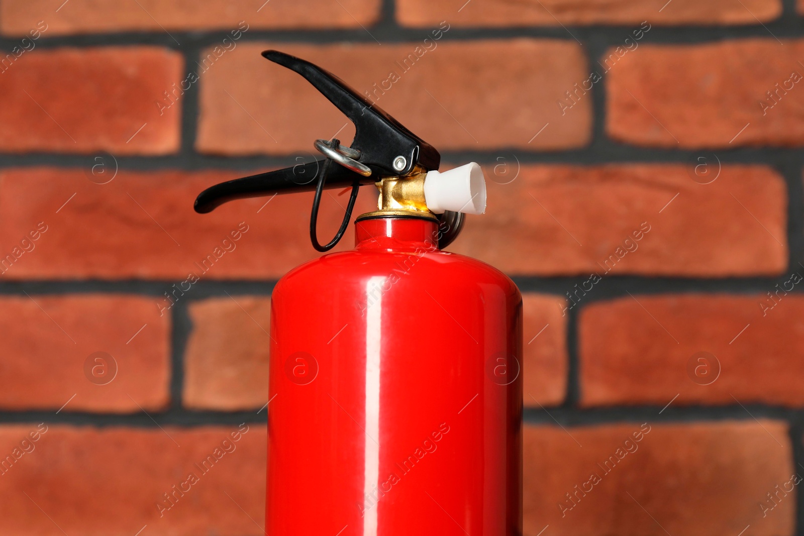 Photo of One red fire extinguisher near brick wall, closeup