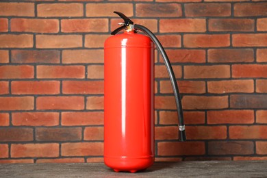 Photo of One red fire extinguisher near brick wall