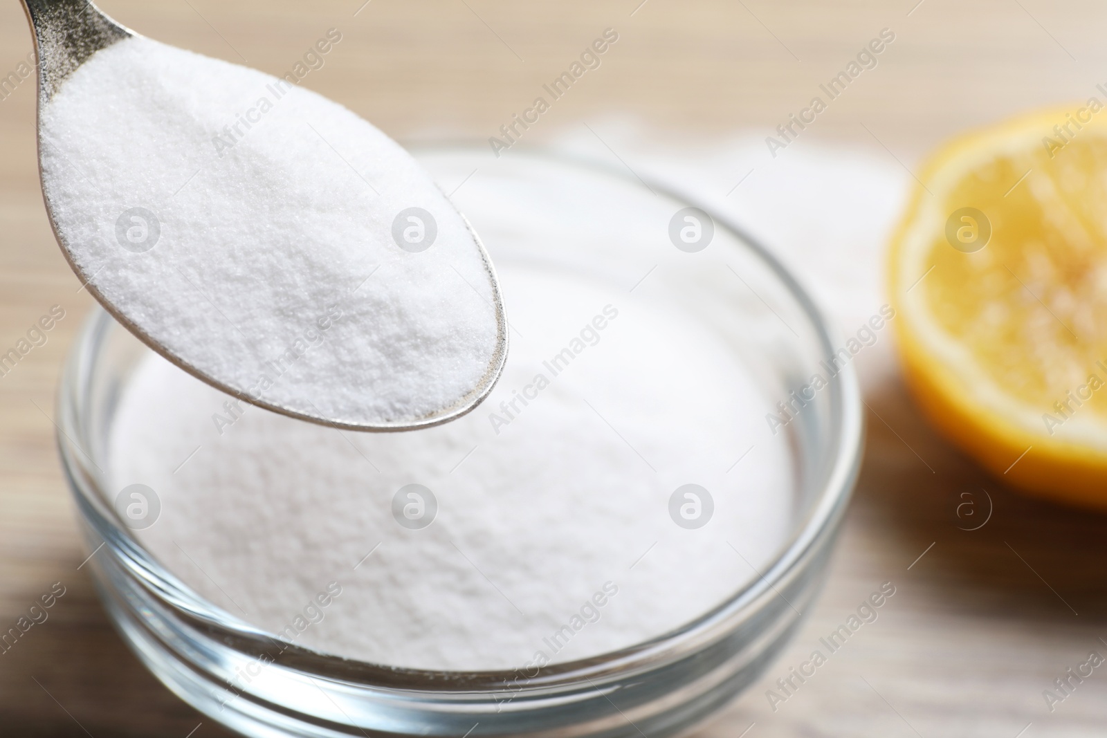 Photo of Taking baking soda from bowl at wooden table, closeup