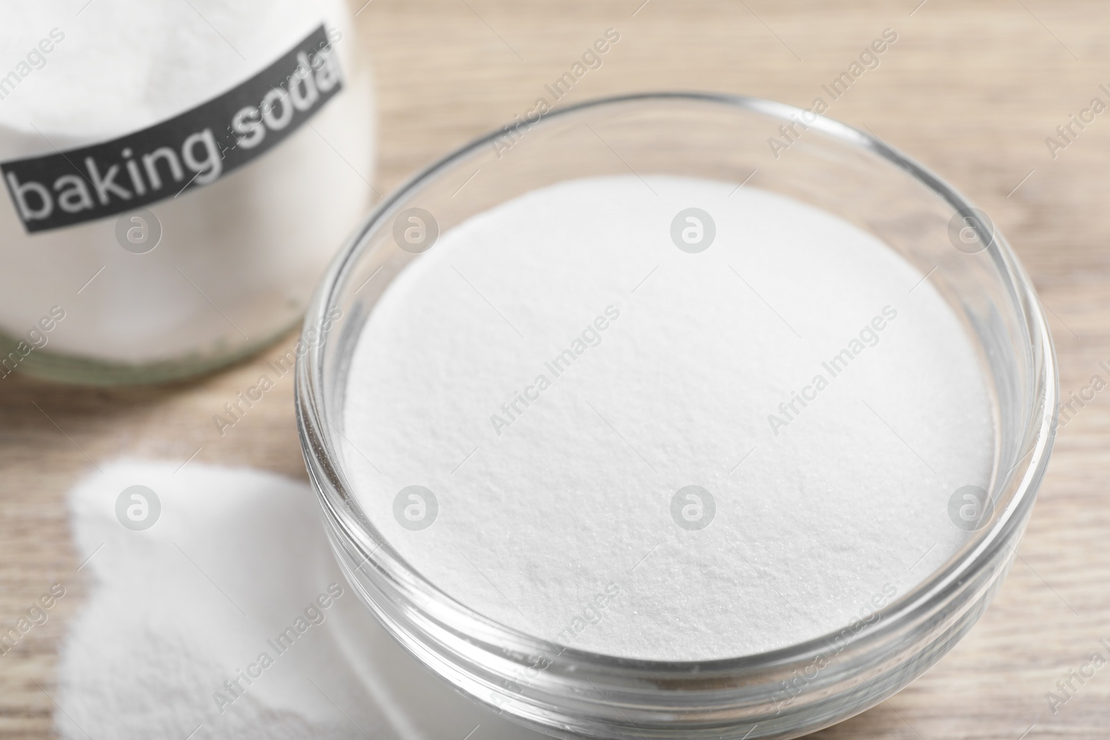 Photo of Baking soda in glass bowl on wooden table, closeup