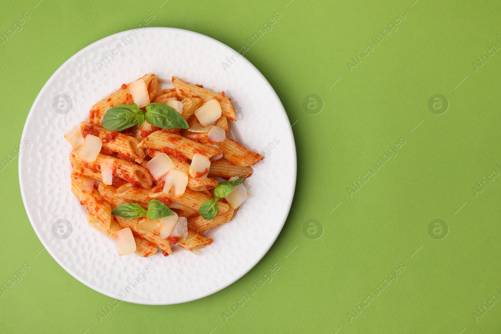 Photo of Tasty pasta with tomato sauce, cheese and basil on green background, top view. Space for text