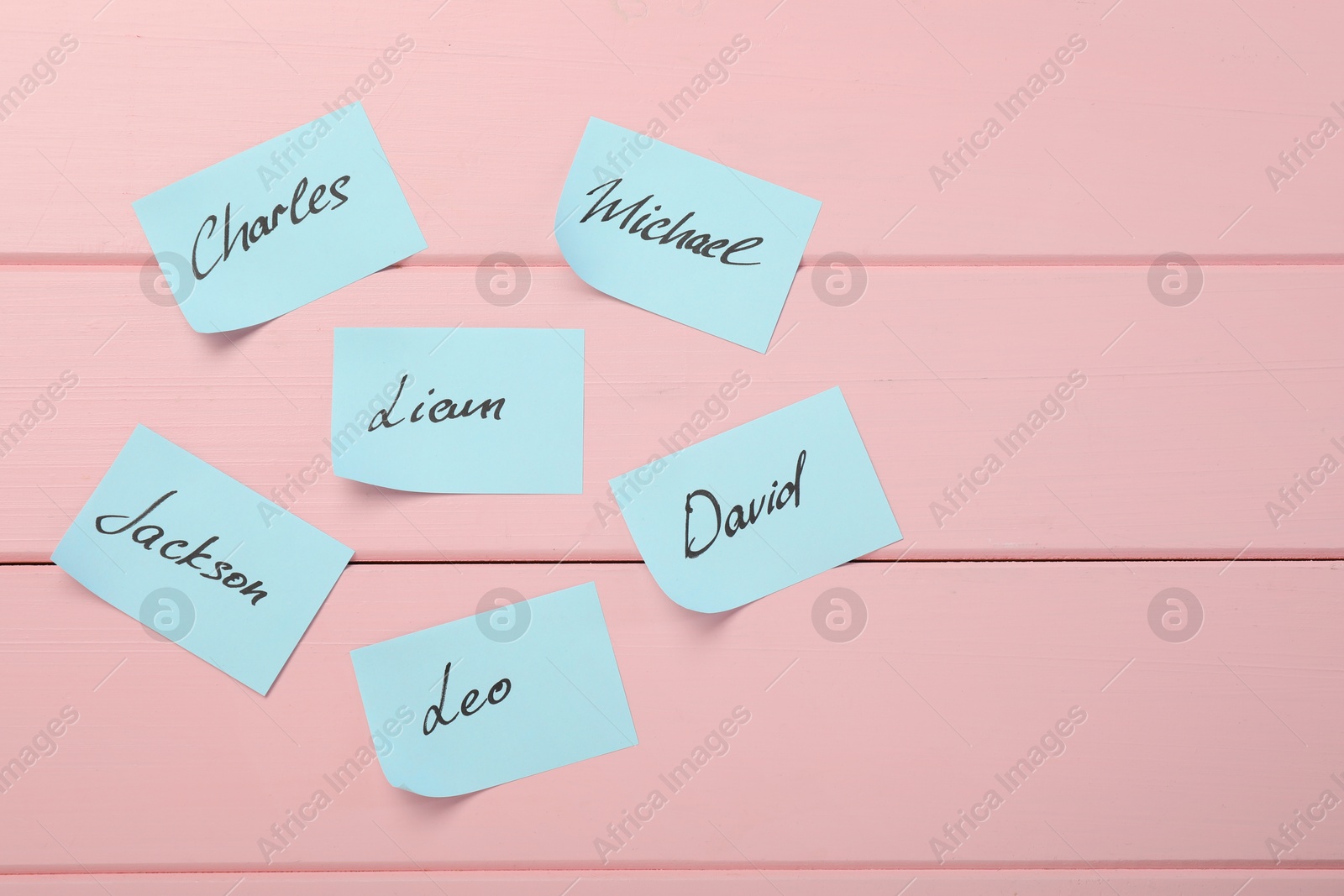 Photo of Choosing baby's name. Paper stickers with different names on pink wooden background, flat lay. Space for text