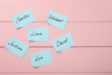 Choosing baby's name. Paper stickers with different names on pink wooden background, flat lay. Space for text