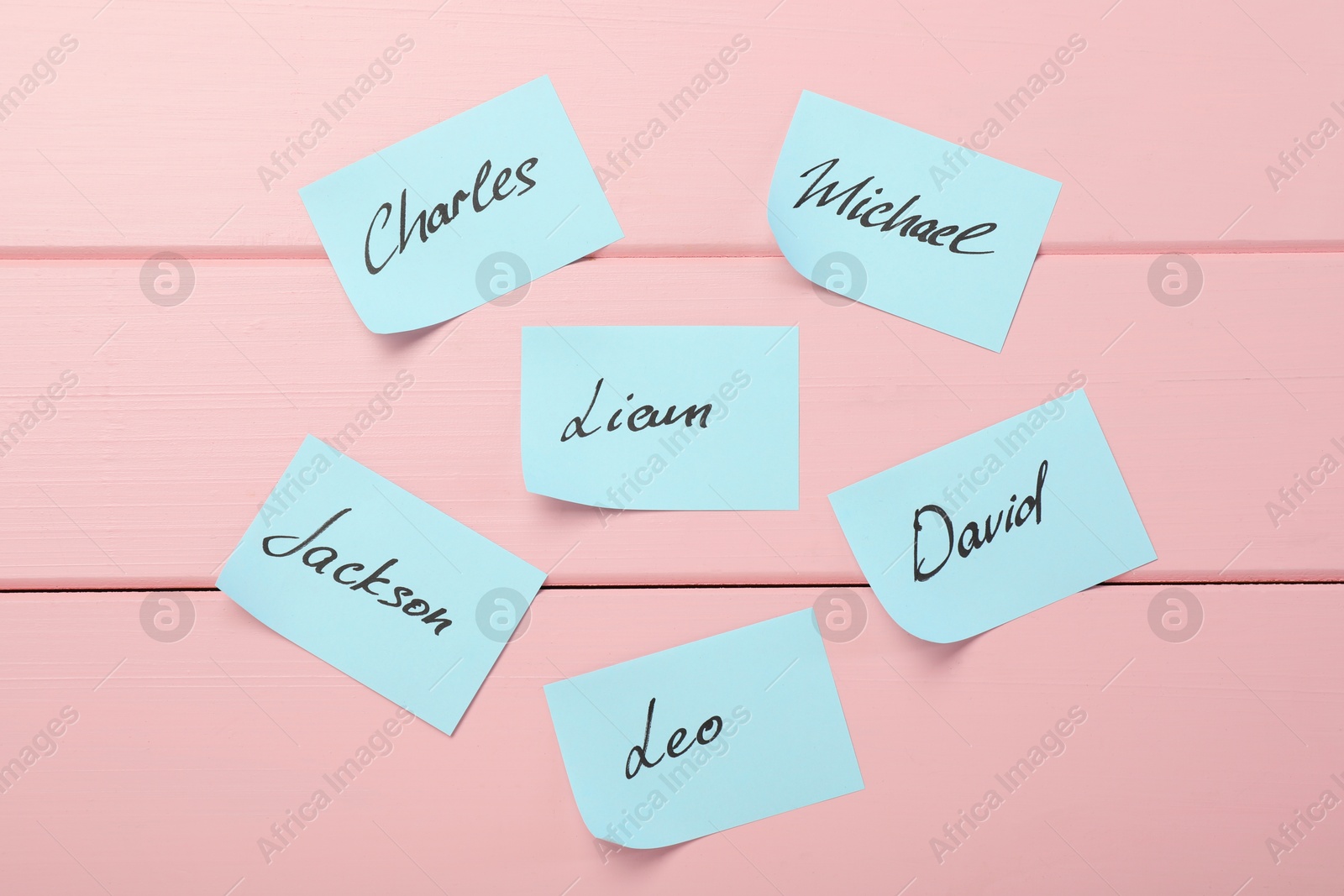 Photo of Paper stickers with different names on pink wooden background, flat lay. Choosing baby's name