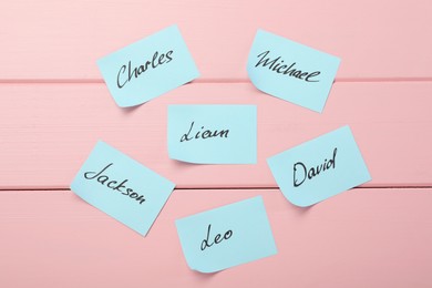 Photo of Paper stickers with different names on pink wooden background, flat lay. Choosing baby's name