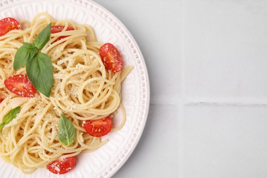 Photo of Tasty pasta with tomato, cheese and basil on white tiled table, top view. Space for text