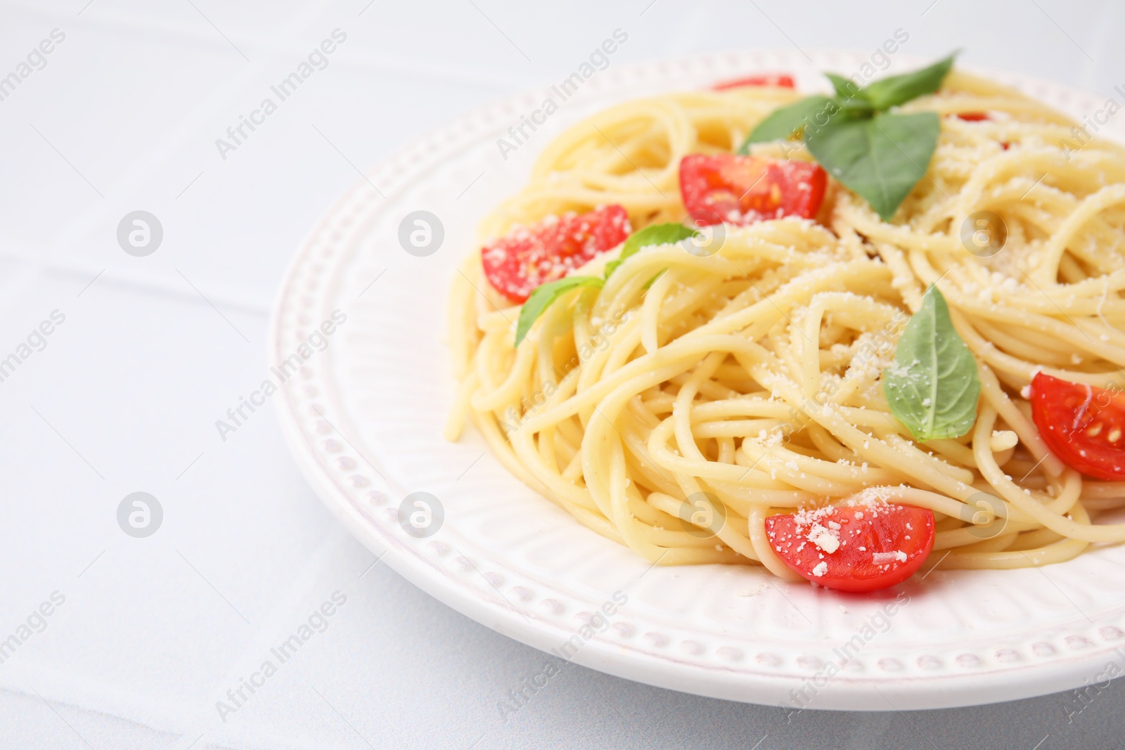 Photo of Tasty pasta with tomato, cheese and basil on white tiled table, closeup