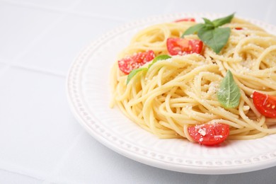 Photo of Tasty pasta with tomato, cheese and basil on white tiled table, closeup