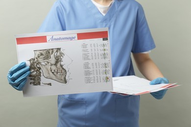 Photo of Doctor with visualization of human maxillofacial section for dental analysis printed on papers against grey background, closeup. Cast of teeth