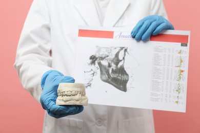 Photo of Doctor holding dental model with jaws and visualization of human maxillofacial section for dental analysis printed on paper against pink background, closeup. Cast of teeth