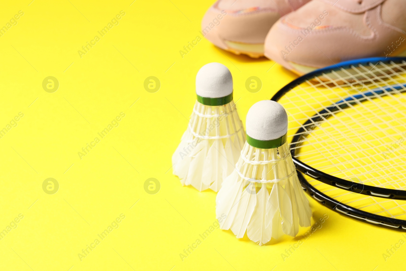 Photo of Feather badminton shuttlecocks, rackets and sneakers on yellow background, closeup. Space for text