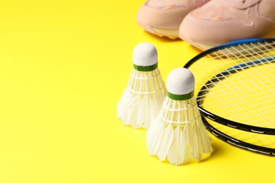 Feather badminton shuttlecocks, rackets and sneakers on yellow background, closeup. Space for text
