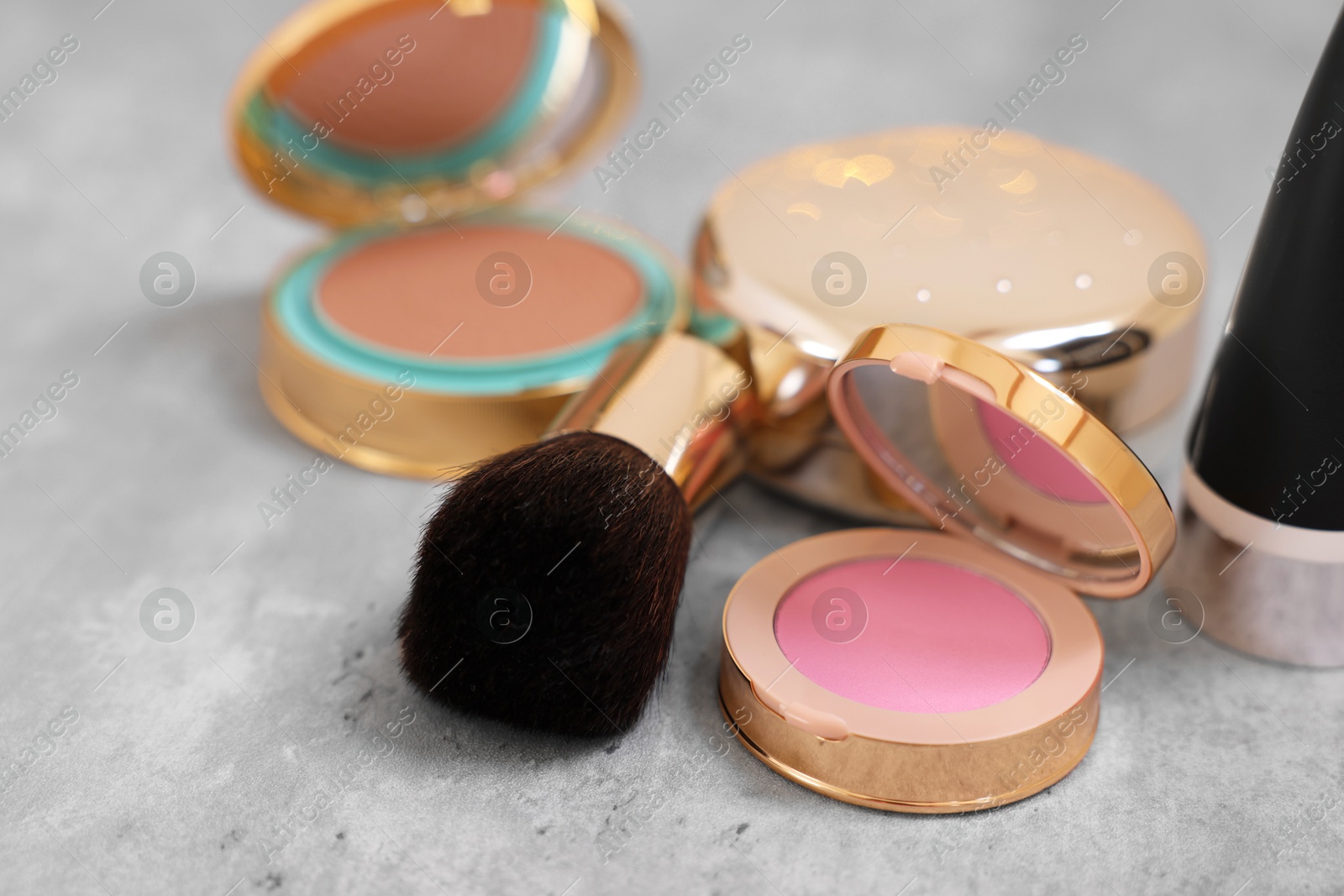 Photo of Face blusher and other cosmetic products on grey textured table, closeup