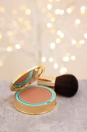 Photo of Face bronzer on grey textured table against blurred lights. Space for text