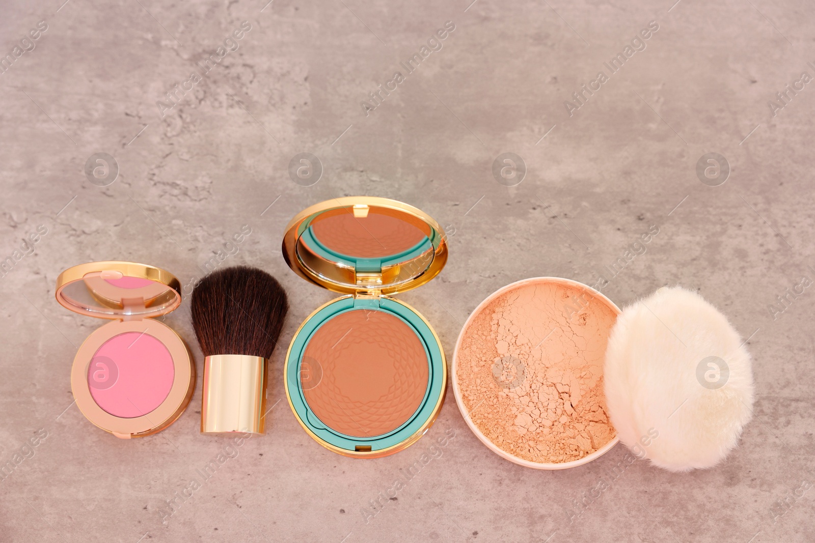 Photo of Bronzer, powder, blusher and brush on grey textured table, flat lay. Space for text