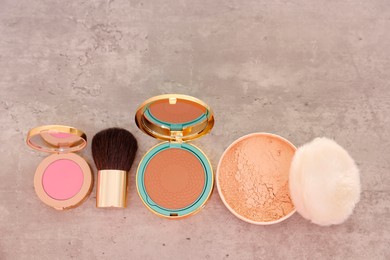 Photo of Bronzer, powder, blusher and brush on grey textured table, flat lay. Space for text