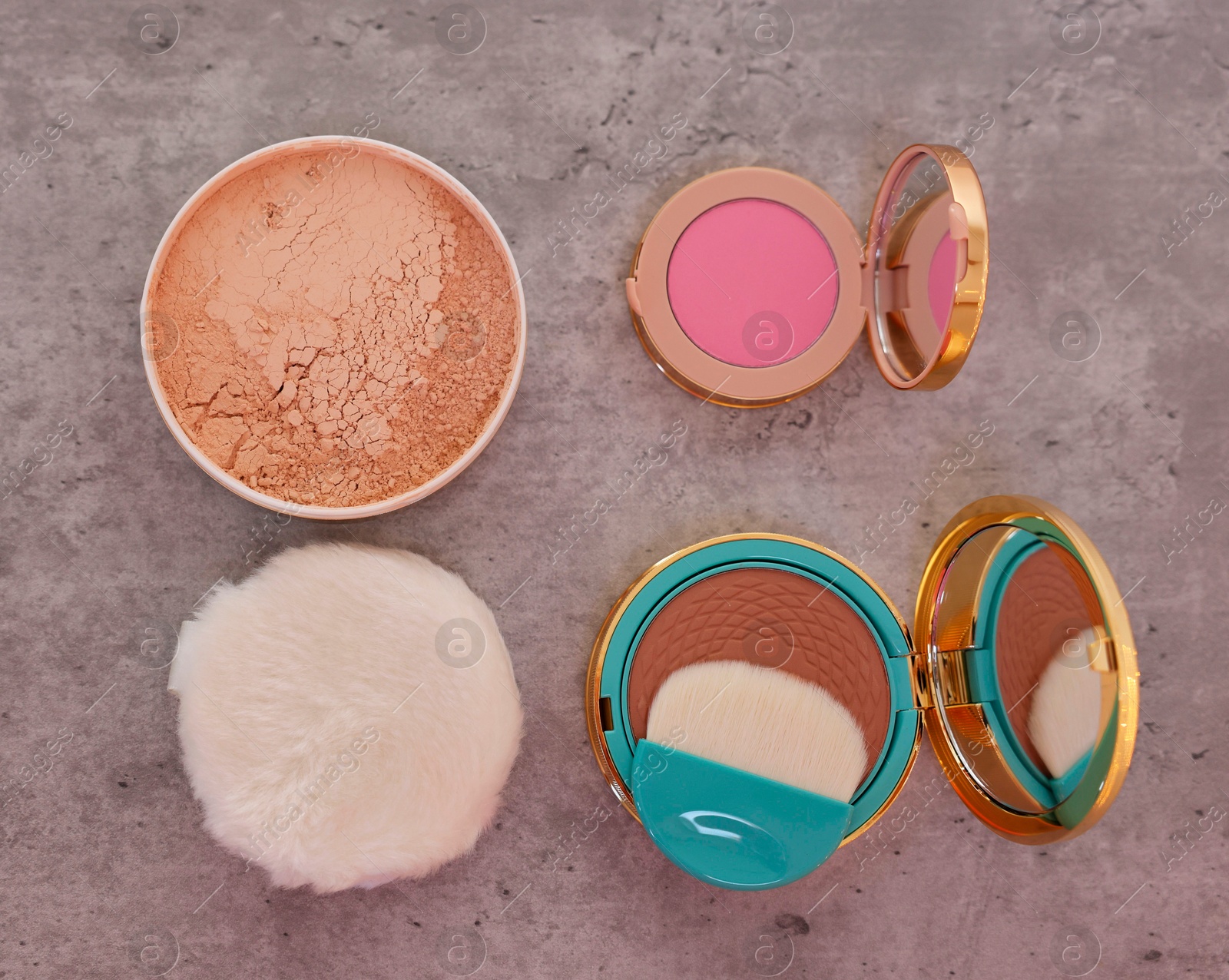 Photo of Bronzer, powder, blusher and brush on grey textured table, flat lay