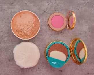 Bronzer, powder, blusher and brush on grey textured table, flat lay