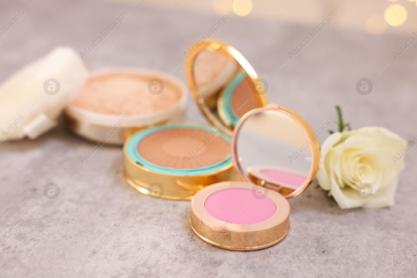 Photo of Composition with bronzer, blusher and rose flower on grey textured table, closeup