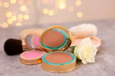 Photo of Composition with bronzer, blusher and rose flower on grey textured table, closeup