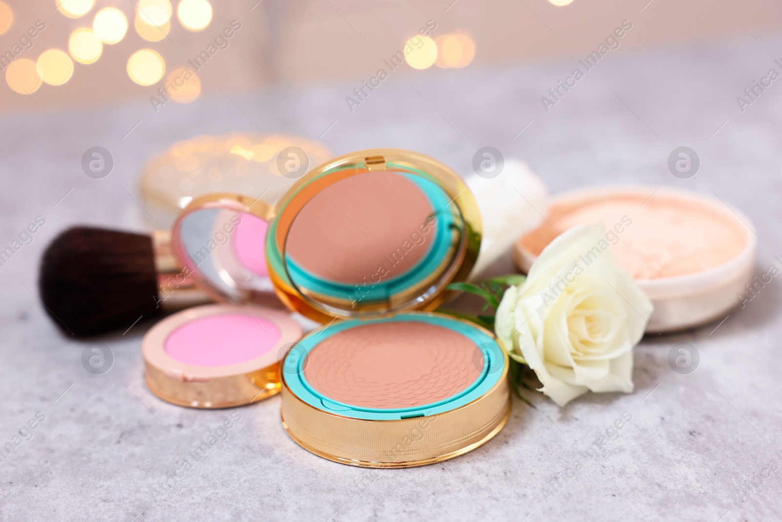 Photo of Composition with bronzer, blusher and rose flower on grey textured table, closeup