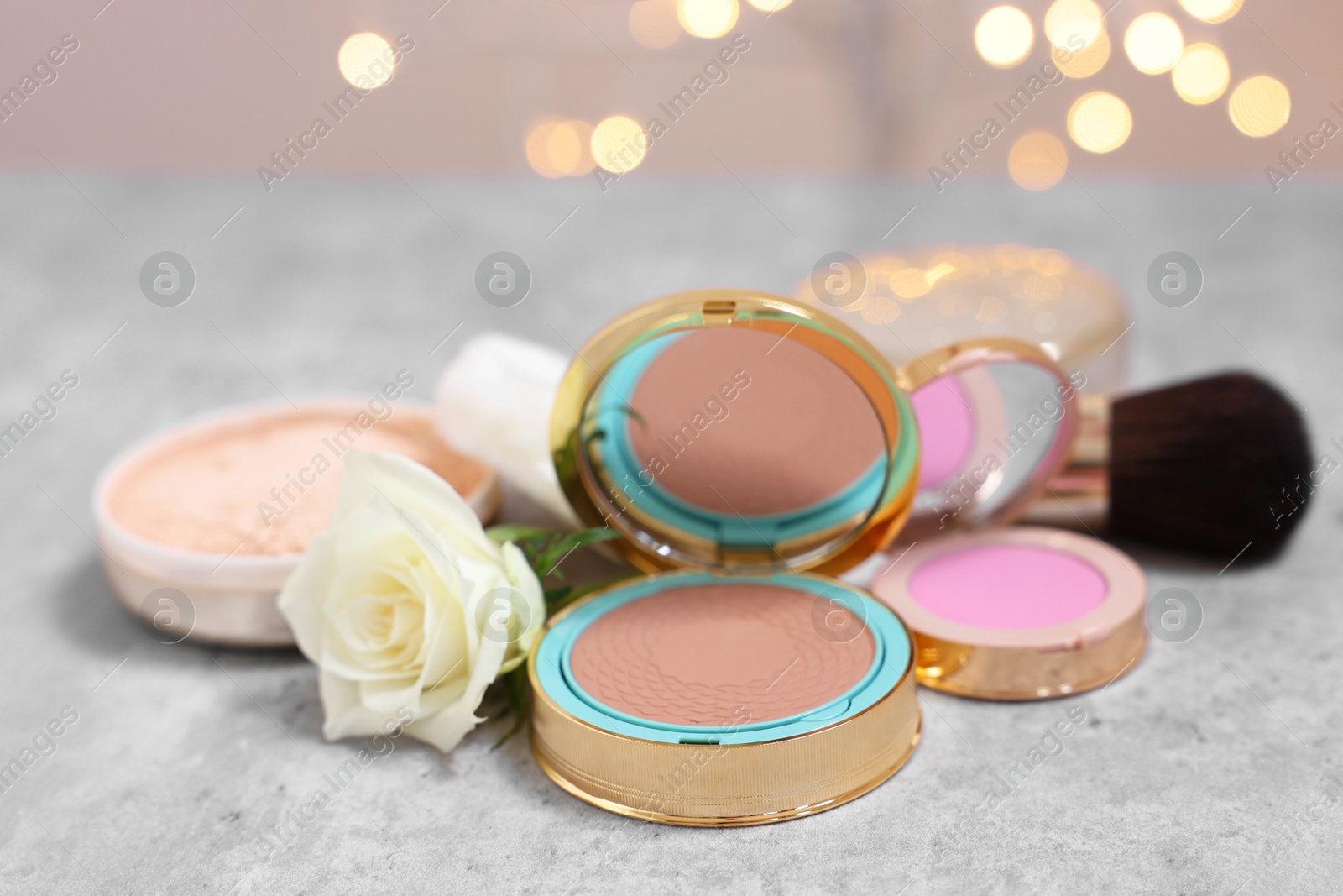 Photo of Composition with bronzer, blusher and rose flower on grey textured table, closeup