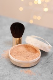 Face powder and brush on grey textured table against blurred lights