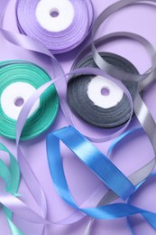 Photo of Ribbon reels in different colors on violet background, flat lay