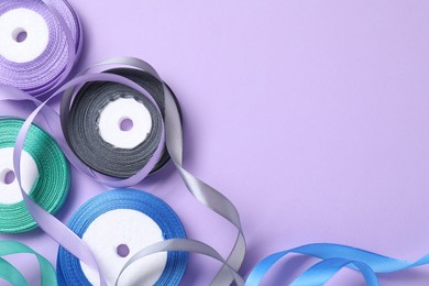 Ribbon reels in different colors on violet background, flat lay. Space for text