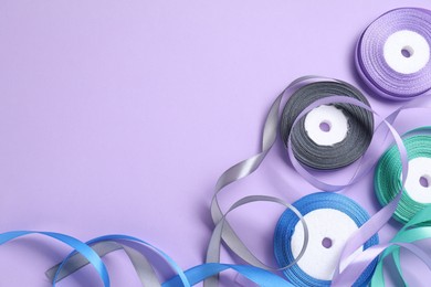 Ribbon reels in different colors on violet background, flat lay. Space for text