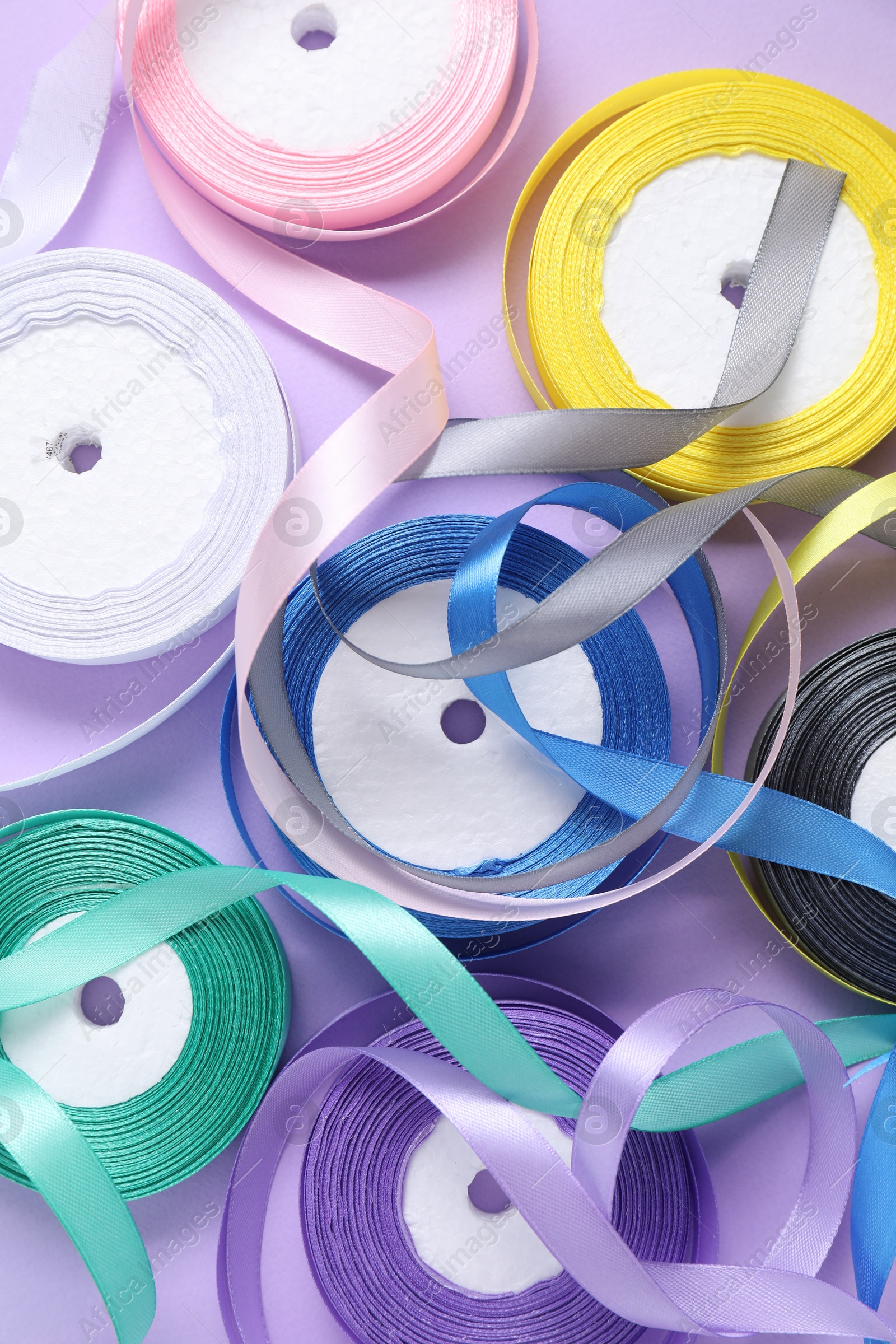 Photo of Ribbon reels in different colors on violet background, flat lay