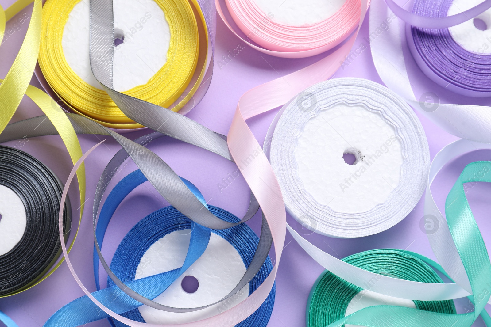 Photo of Ribbon reels in different colors on violet background, flat lay