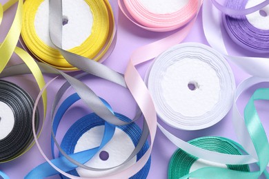 Photo of Ribbon reels in different colors on violet background, flat lay