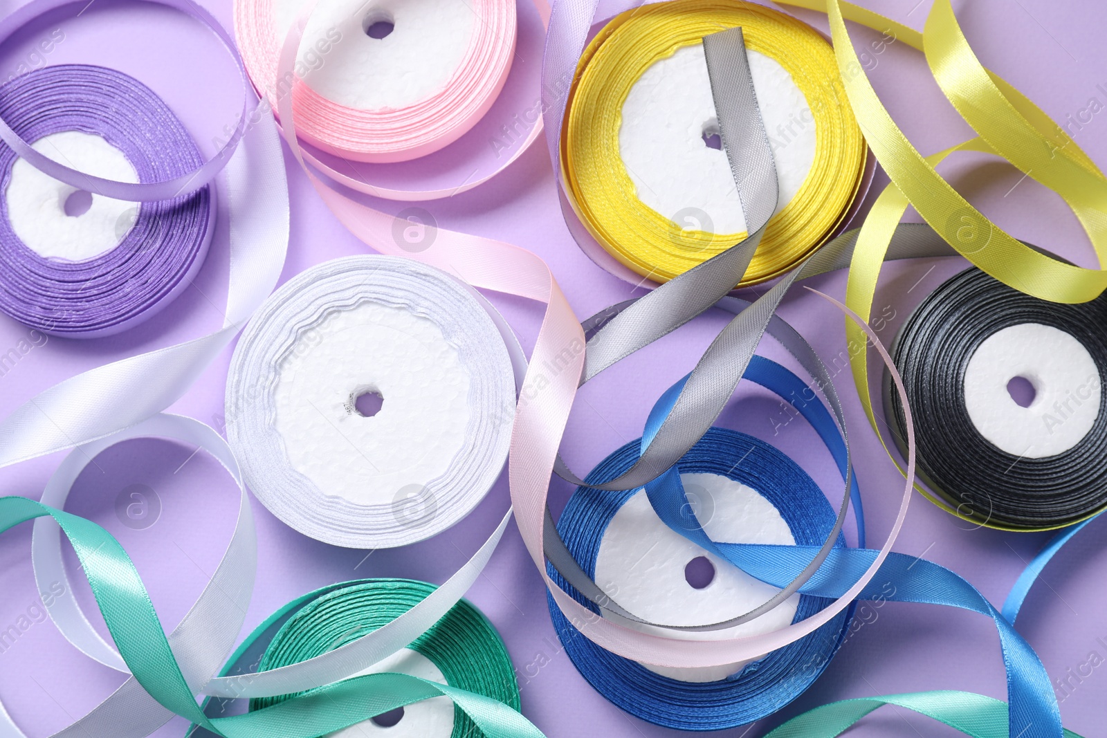 Photo of Ribbon reels in different colors on violet background, flat lay