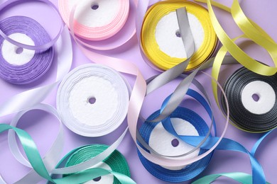 Ribbon reels in different colors on violet background, flat lay