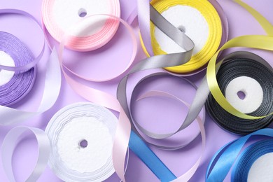 Ribbon reels in different colors on violet background, flat lay