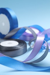 Photo of Ribbon reels in different colors on light blue background, closeup