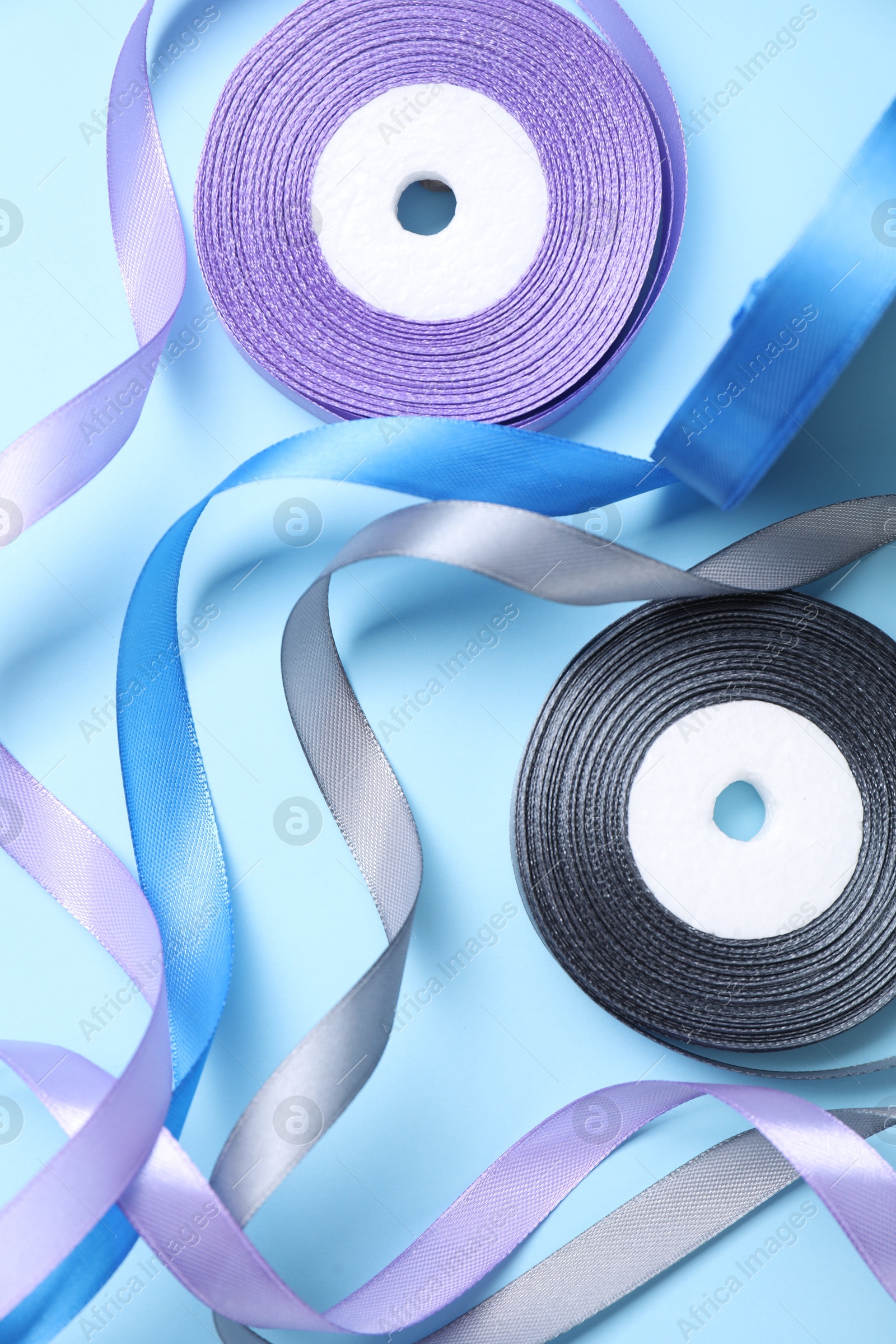 Photo of Ribbon reels in different colors on light blue background, flat lay