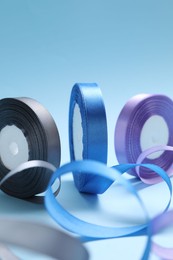 Photo of Ribbon reels in different colors on light blue background, closeup