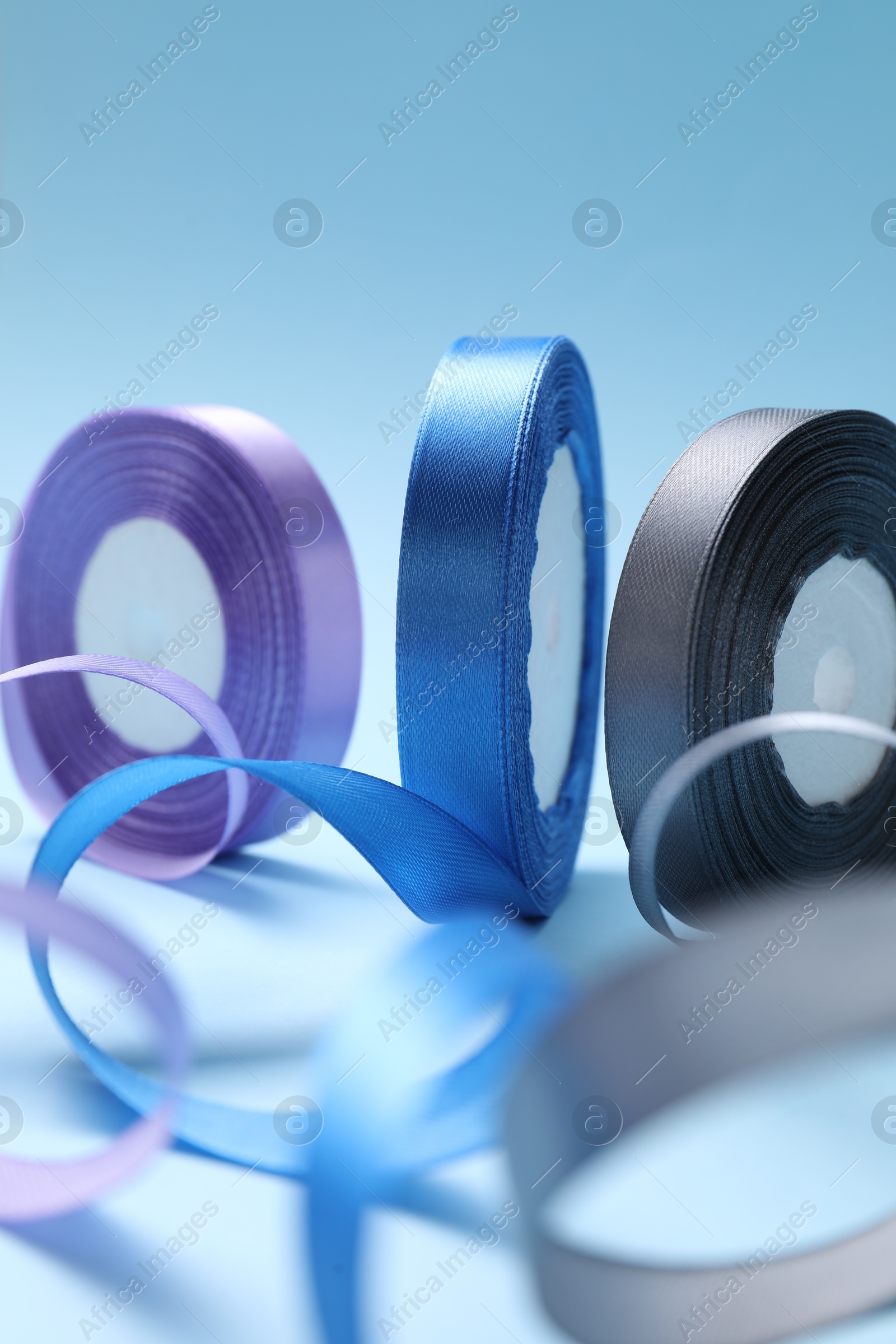 Photo of Ribbon reels in different colors on light blue background, closeup