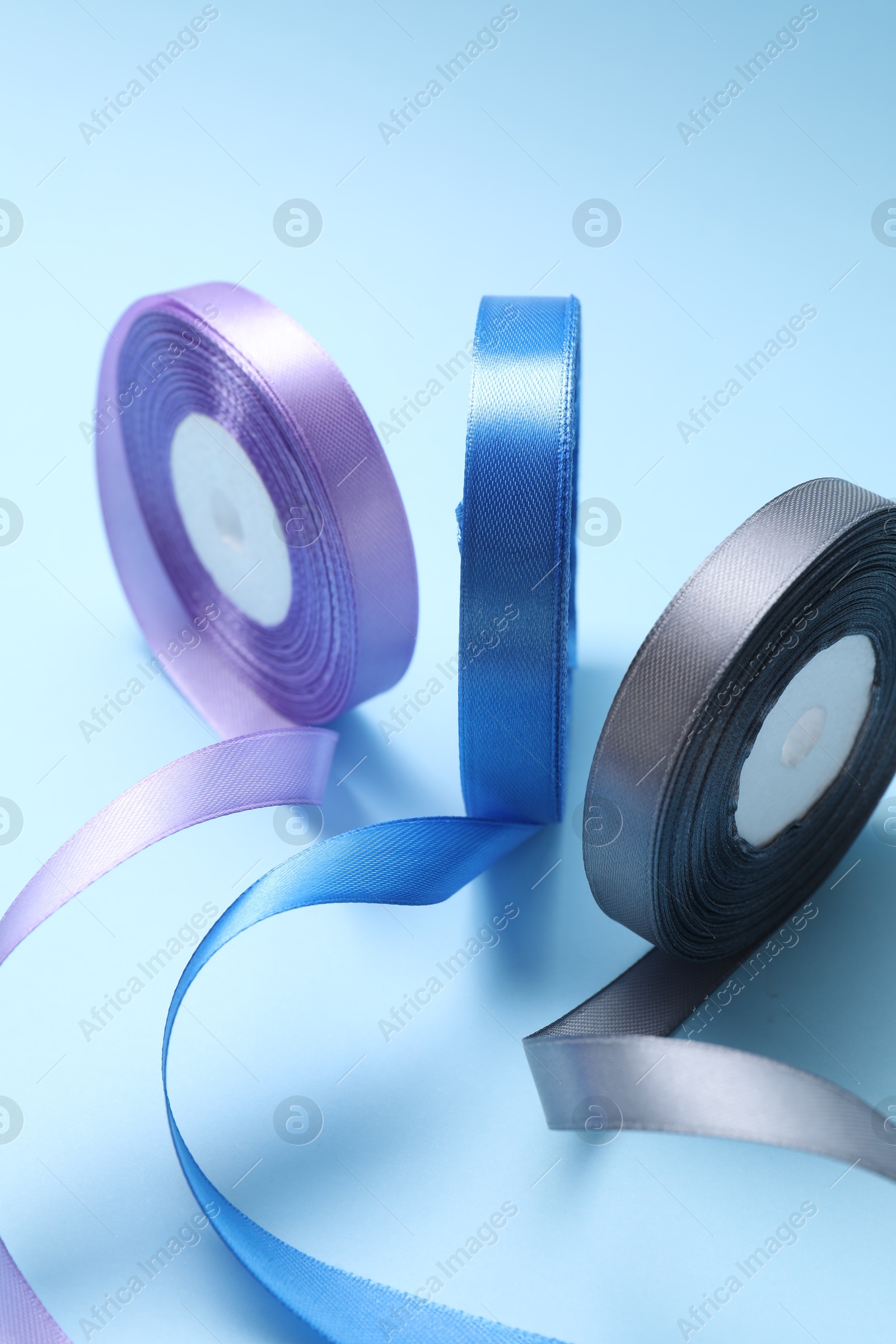 Photo of Ribbon reels in different colors on light blue background, closeup