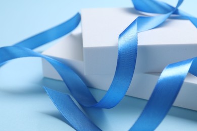 Photo of Beautiful bright ribbon and gift boxes on light blue background, closeup