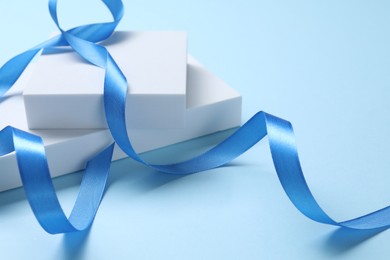 Photo of Beautiful bright ribbon and gift boxes on light blue background