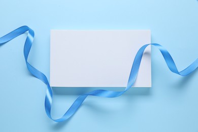 Beautiful bright ribbon and gift box on light blue background, flat lay