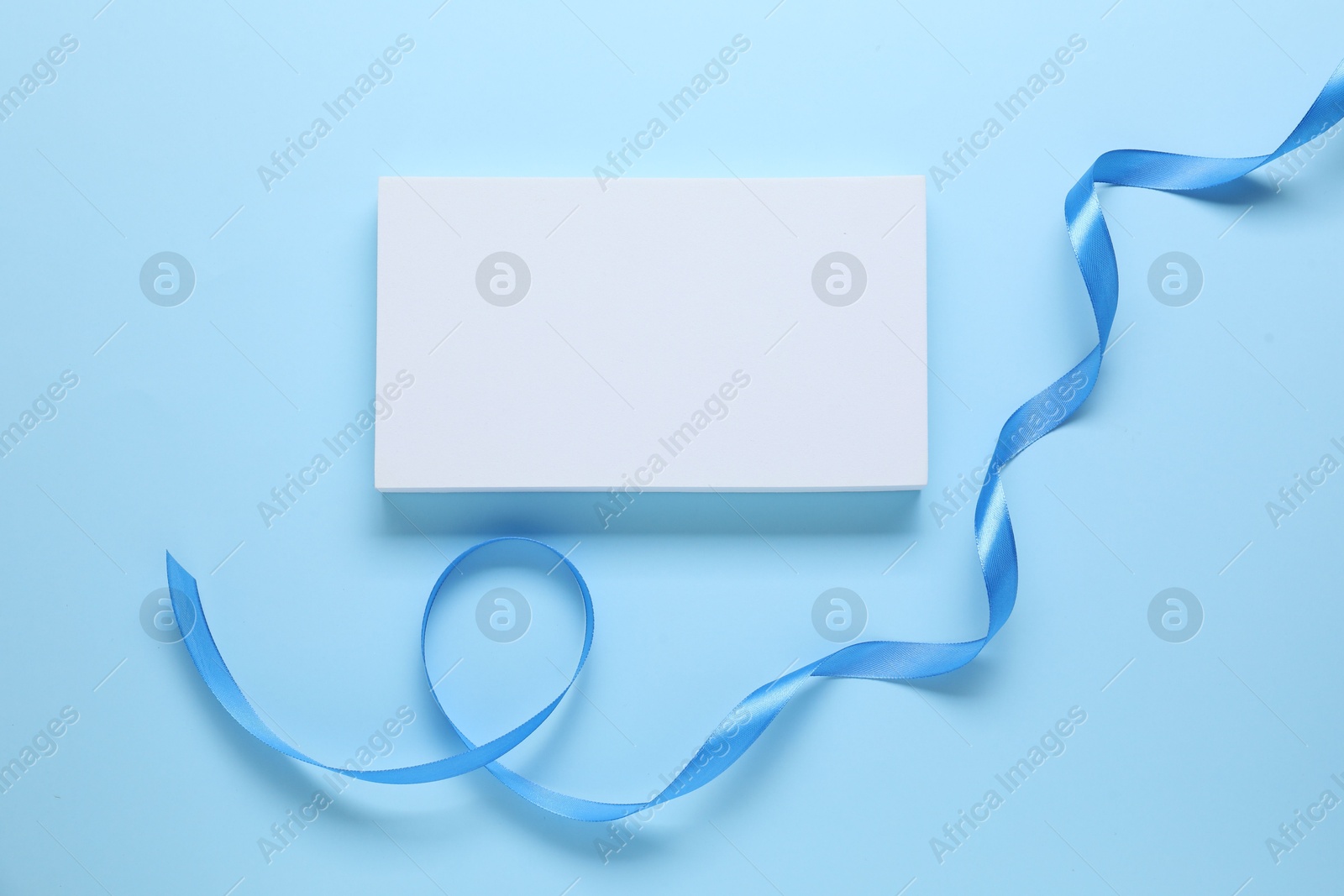 Photo of Beautiful bright ribbon and gift box on light blue background, flat lay