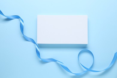 Beautiful bright ribbon and gift box on light blue background, flat lay