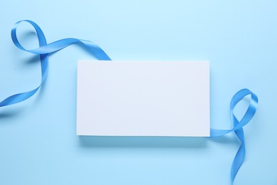 Beautiful bright ribbon and gift box on light blue background, flat lay