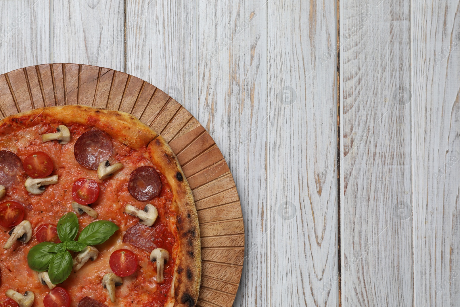 Photo of Delicious pizza with salami, tomatoes, mushrooms and basil on wooden table, top view. Space for text