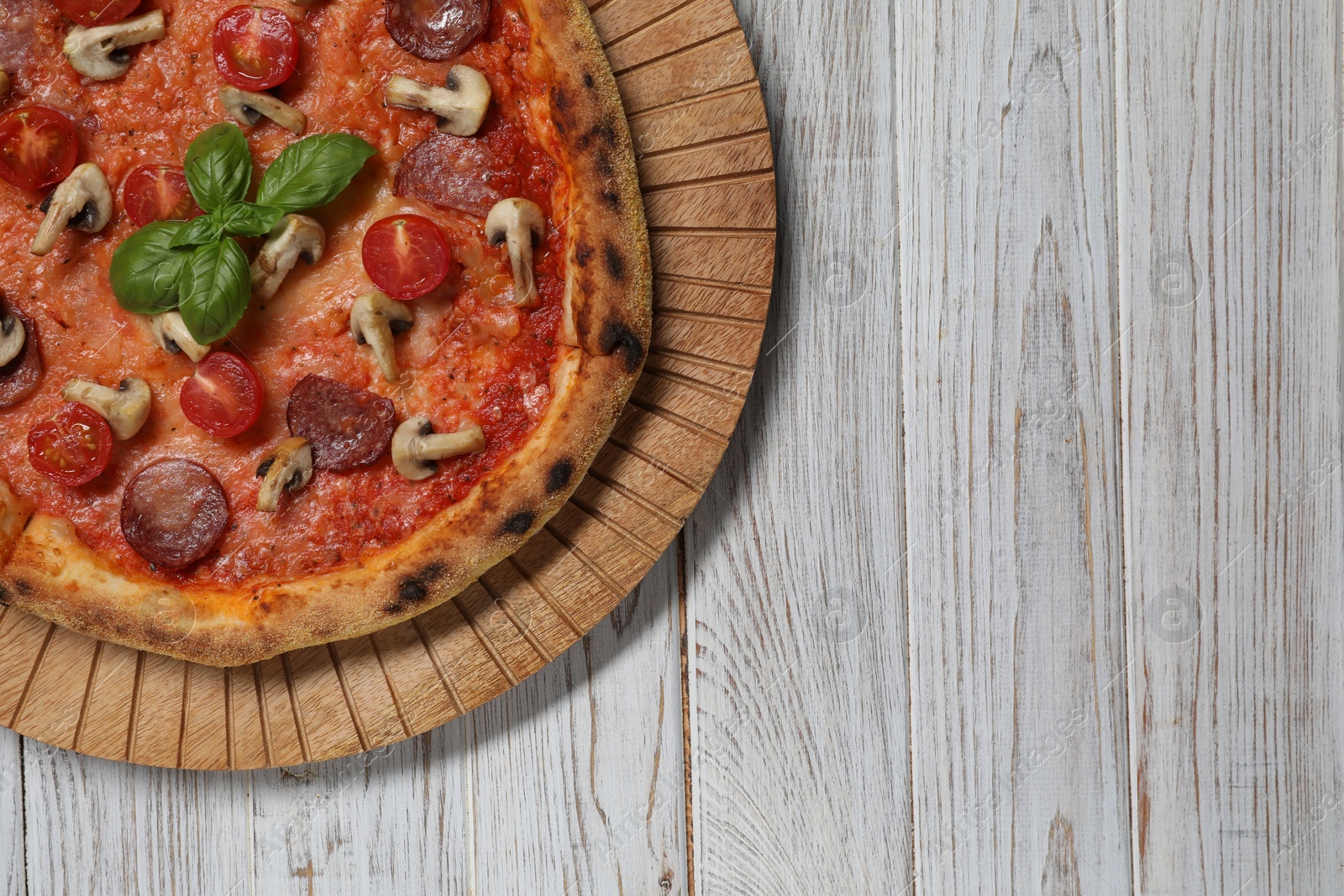 Photo of Delicious pizza with salami, tomatoes, mushrooms and basil on wooden table, top view. Space for text