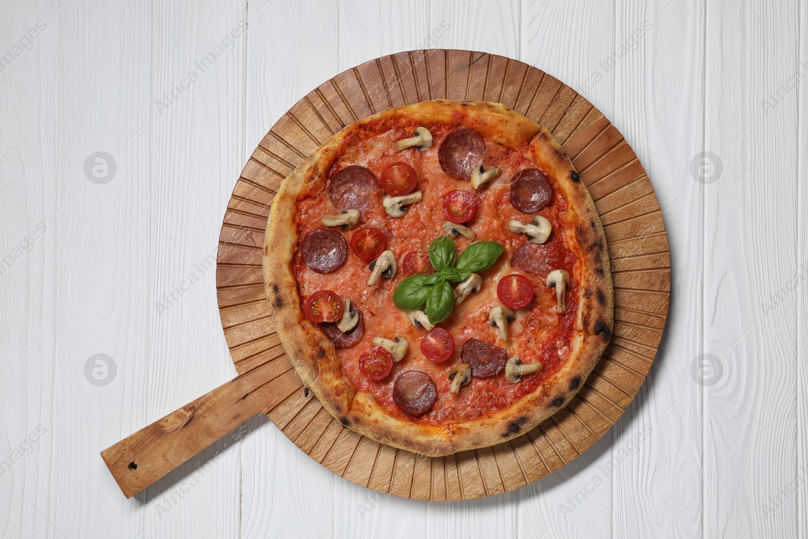 Photo of Delicious pizza with salami, tomatoes, mushrooms and basil on white wooden table, top view